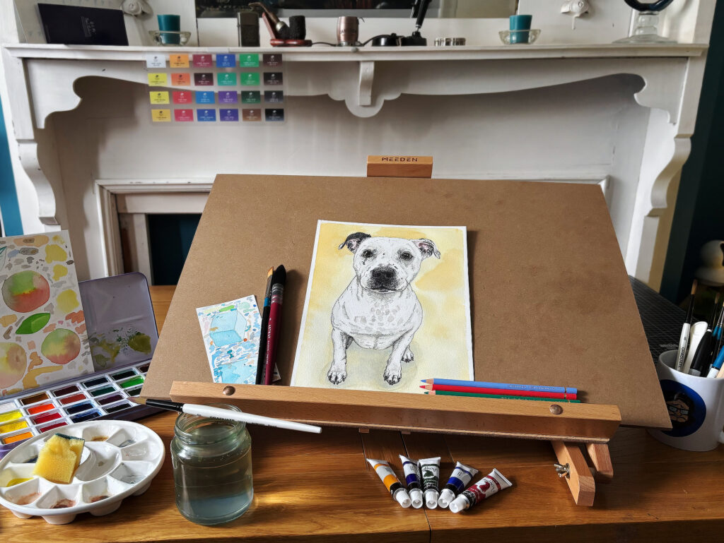 The Shimmus Studios drawing table with a dog portrait, paints and art materials.