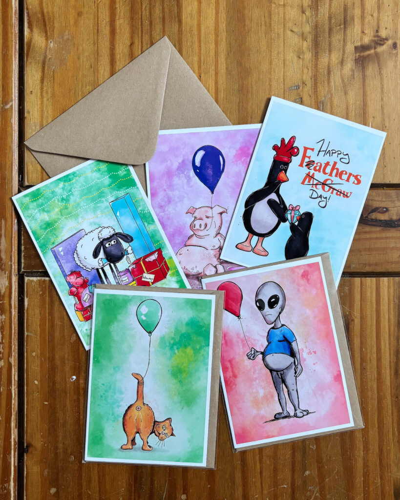 A selection of illustrated Shimmus Studios greeting cards arranged on the drawing table.